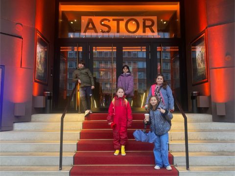 Fünf Kinder stehen vor der Astor Lounge auf einer Treppe.