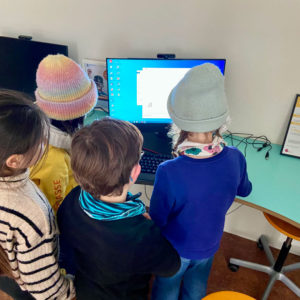 Vier Kinder stehen vor einem Computer und gucken gespannt auf den Monitor.