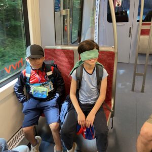 Zwei Kinder sitzen in der U-Bahn. Eines hat die Augen verbunden.