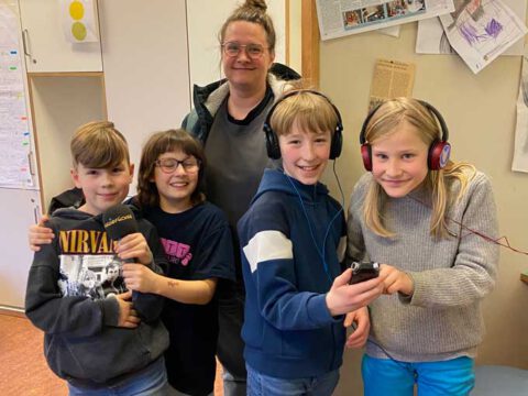 Vier Kinder mit Aufnahmegerät, Kopfhörern und Mikrofon und eine Frau