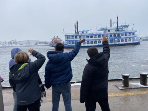 Drei Kinder von hinten, die einem Schiff zuwinken