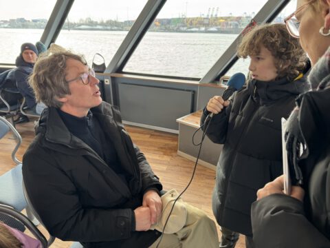 Zwei Kinder interviewen Peter Feddersen auf einer HADAG Fähre