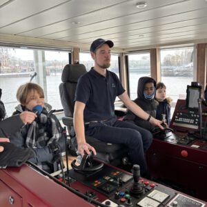 Kapitän im Steuerhaus der HADAG Fähre, hinter ihm drei Kinder