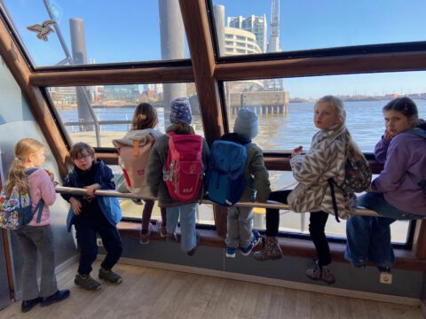 Kinder schauen durch große Fenster auf die Elbe und die Hafencity