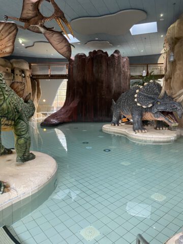 Blick auf das "Dinobecken" im Schwimmbad Festland mit zwei Dinosauriern und Baumstumpf im Hintergrund